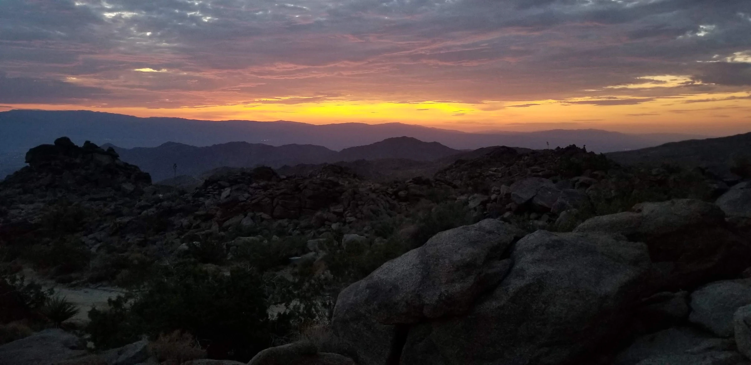 Golden sky above the boulders and layered mountain views at Viva Las Rocas