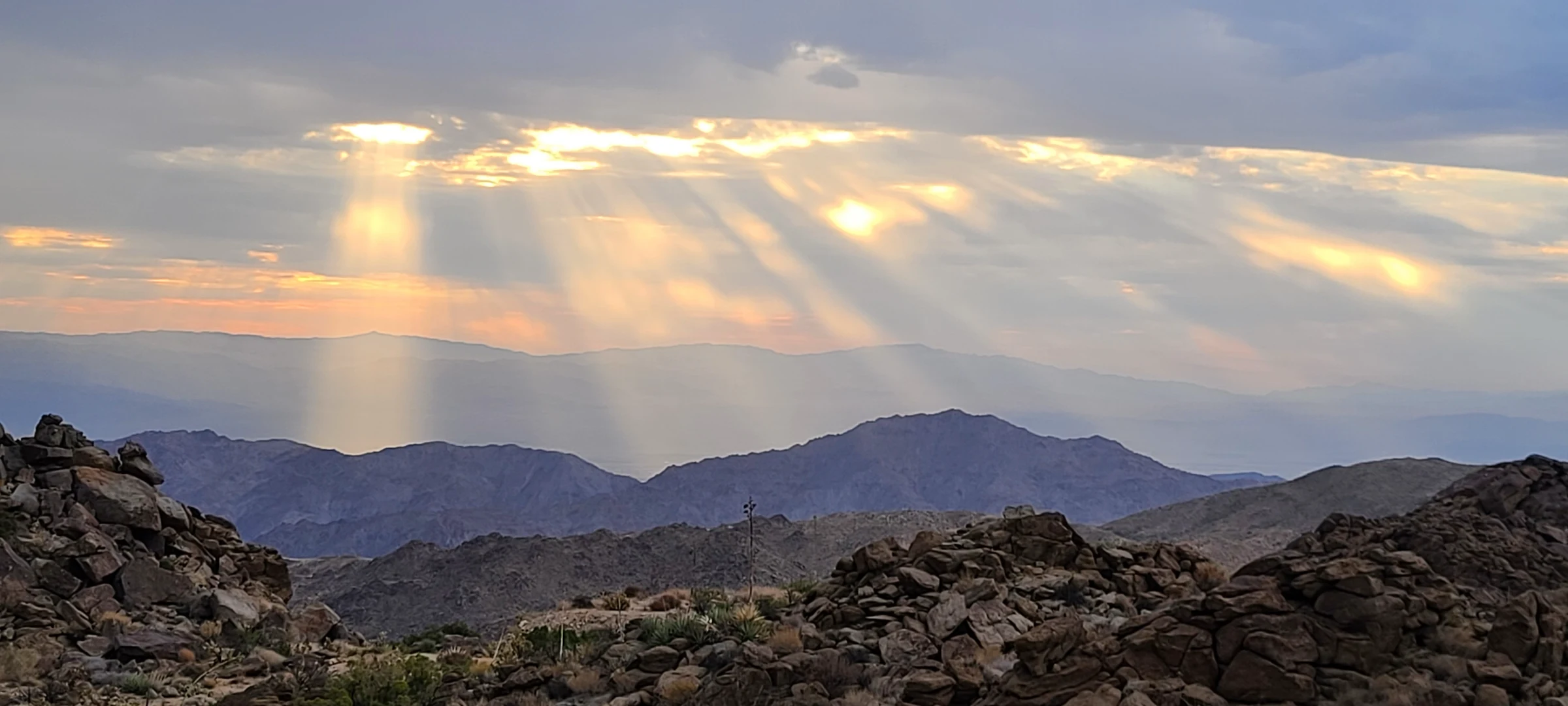 Shafts of sunlight crossing layered mountain ridges beyond the estate’s boulders